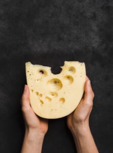 close up hand holding maasdam cheese against black textured backdrop